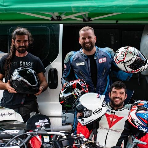 photo of three bikers smiling and holding bike helmets