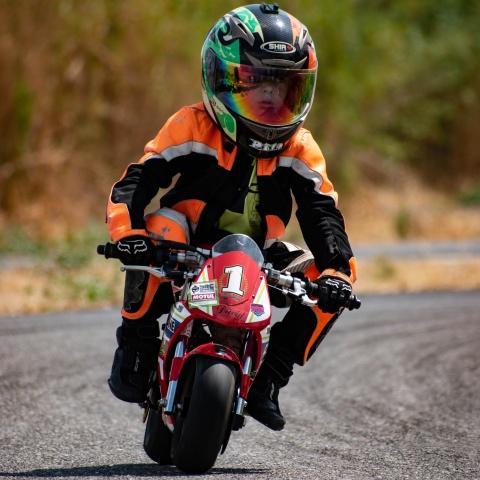 kid biker riding small red sports bike in race track
